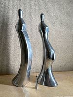 Two tall abstract aluminum human figures and small bird figure group