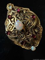 Front view of gold filigree pendant-brooch showing central opal, surrounding rubies, top opal, intricate openwork