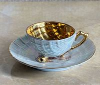 Cup on saucer showing gold interior and iridescent finish