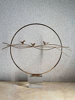 Full view of gold-tone circular bird sculpture on clear base