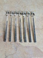 Seven matching sterling silver cocktail forks laid out flat, showing full design