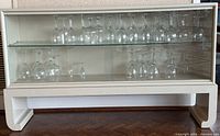 Full view of white cabinet with sliding glass doors and glass shelf inside