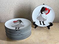 Stack of 12 plates with one plate on stand displaying design