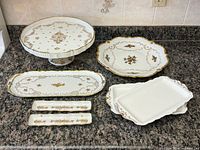 Group shot of all seven white and gold porcelain serving pieces on countertop