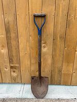 Full view of shovel leaning on wood fence