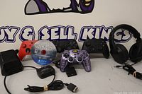 Group shot of all items: two Xbox controllers, purple wired controller, Hogwarts Legacy disc, headset, charging dock, RadioShack modulator, cables
