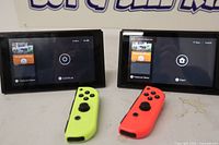 Front view two Switch consoles powered on with neon yellow left and neon red right Joy-Con controllers