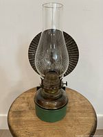 Front view of complete oil lamp showing green tin base, brown glass font, clear chimney, ribbed reflector
