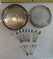 Two round silver-plated hot plates and 12 teaspoons displayed on countertop
