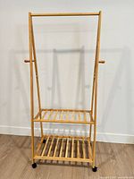 Front view of bamboo garment rack showing hanging rod, two slatted shelves, wheels