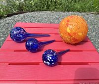 Bee ball and three watering globes grouped on red surface