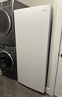 Closed front view of upright freezer beside washer/dryer