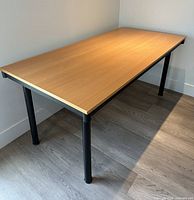 Oblique view of full table showing light wood top and black legs