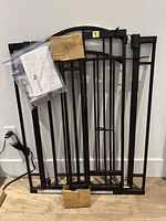 Folded black metal gate with cardboard-wrapped sections leaning against wall