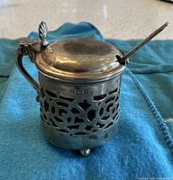 Sterling silver mustard pot with pierced body, lid closed, spoon inserted