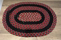 Top view of oval braided rug showing red, grey, black pattern