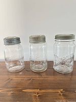 Three vintage quart canning jars side by side showing brands and lids
