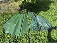 Three green PVC tree watering bags on grass, one opened, one folded, one sealed