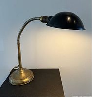 Side view of lit gooseneck lamp showing overall form, shade and cord