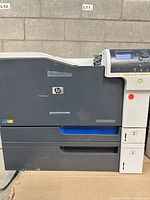 Front view of HP Color LaserJet CP5525 printer showing HP logo, color finish, paper trays 2 and 3, and control panel