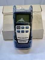 Front view of shrink-wrapped DXL-40D optical power meter standing in front of its white retail box