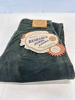 Folded dark green suede pants showing brand patch and paper tags