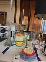 All six items together on table: tall bud vase, hurricane with painted base, cylinder vase, two ceramic canisters, metal bucket and small ceramic cup