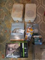 All items laid out: two white outdoor speakers, boxed LED lamp, packaged rope light kit, ACE water timer box, tarp zipper kit