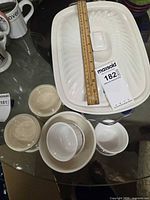 Top view of casserole dish with lid, ramekins and bowls on glass table, MaxSold lot tag visible