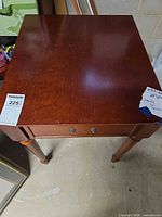 Top view showing square surface, drawer front, turned legs, condition tag