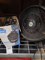 Flotec pump box beside Honeywell fan on shelf