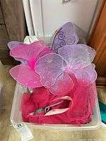 Plastic bin containing pink and purple fairy wings and tutu