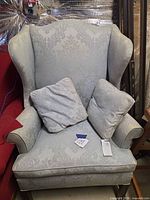 Full view of light blue damask wingback armchair with two pillows and seat cushion