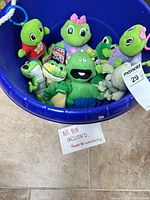 Top view of blue bin containing approximately ten green frog and alligator plush toys
