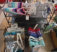 Plastic hangers in boxes and on top of black shoe rack, shows quantity and color variety; black metal shoe rack visible behind