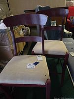 Pair of burgundy wood dining chairs with beige seats showing wear