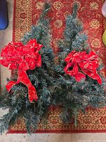 Two small artificial Christmas trees with red bows lying side by side on rug
