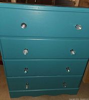 Front view of teal four-drawer dresser showing crystal knobs and overall condition