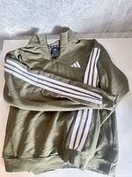 Full view of folded Adidas olive green quarter-zip sweater showing stripe detail and logo