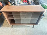 Front view of wood veneer cabinet showing sliding glass doors and interior shelf