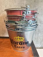 Stack of eight metal beer buckets showing Corona Extra branding on bottom bucket