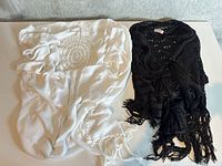 White knit cardigan with crochet medallion and fringe next to black crochet fringed cardigan