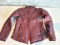 Front view of burgundy quilted down jacket with grey side panels fully zipped