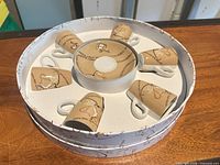 Round gift box opened to show six espresso cups arranged radially around stacked saucers