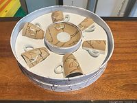 Boxed set showing six cups arranged around central stack of saucers