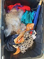 Assorted textiles, blue umbrella, clear garment bag, patterned scarf inside bin