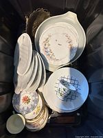 Top view of bin showing round floral platter, stack of white oval plates, pour-spout bowl, metal tray, teacup