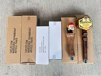 Five tap handles, three boxed, two unboxed (La Chouffe gnome and Maredsous hex) on concrete surface