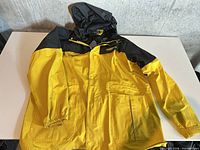 Front view of yellow and black rain jacket laid flat showing overall design