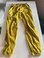 Full view of yellow Ocun climbing pants laid flat on table